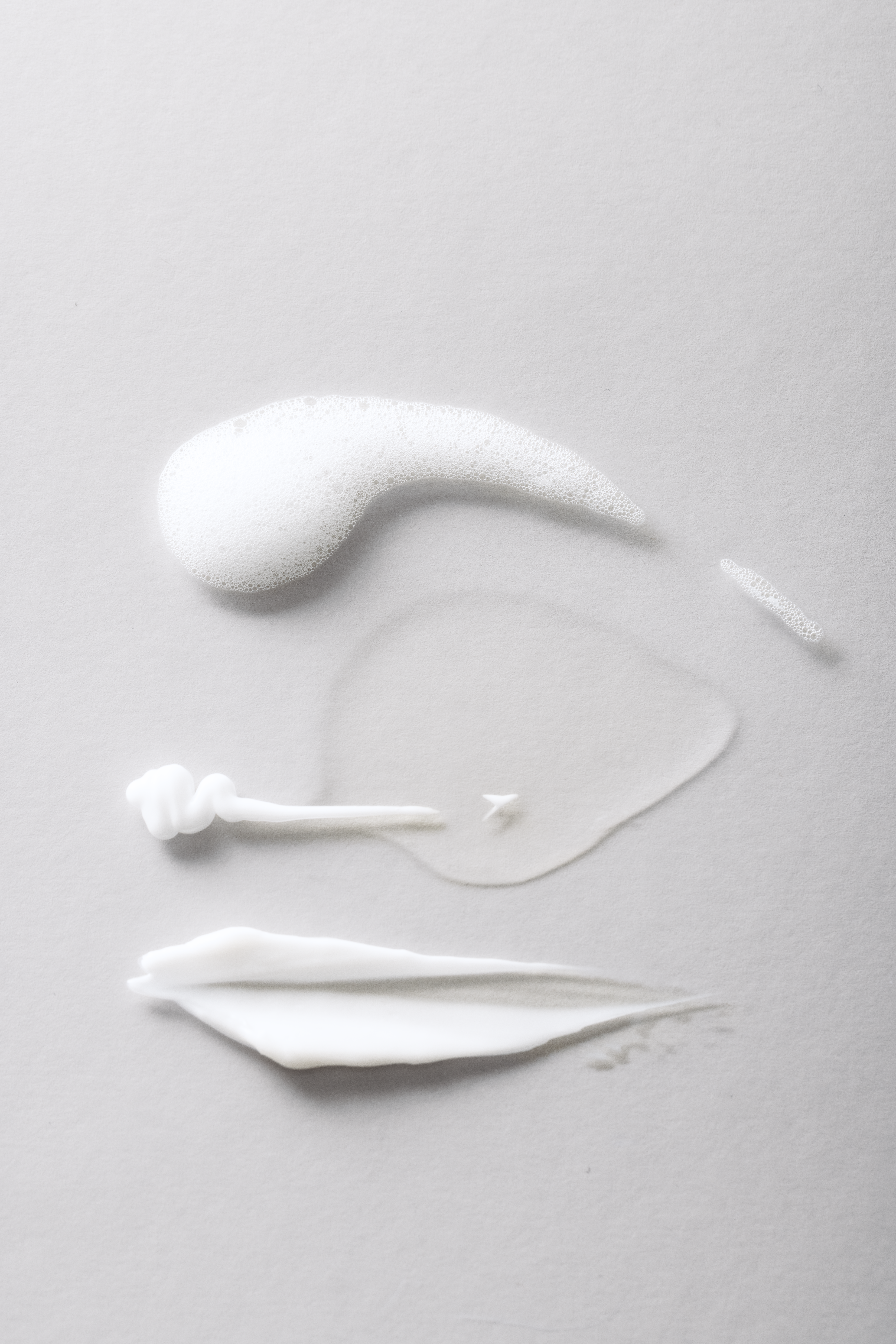 White cream or lotion with application tools on a gray background