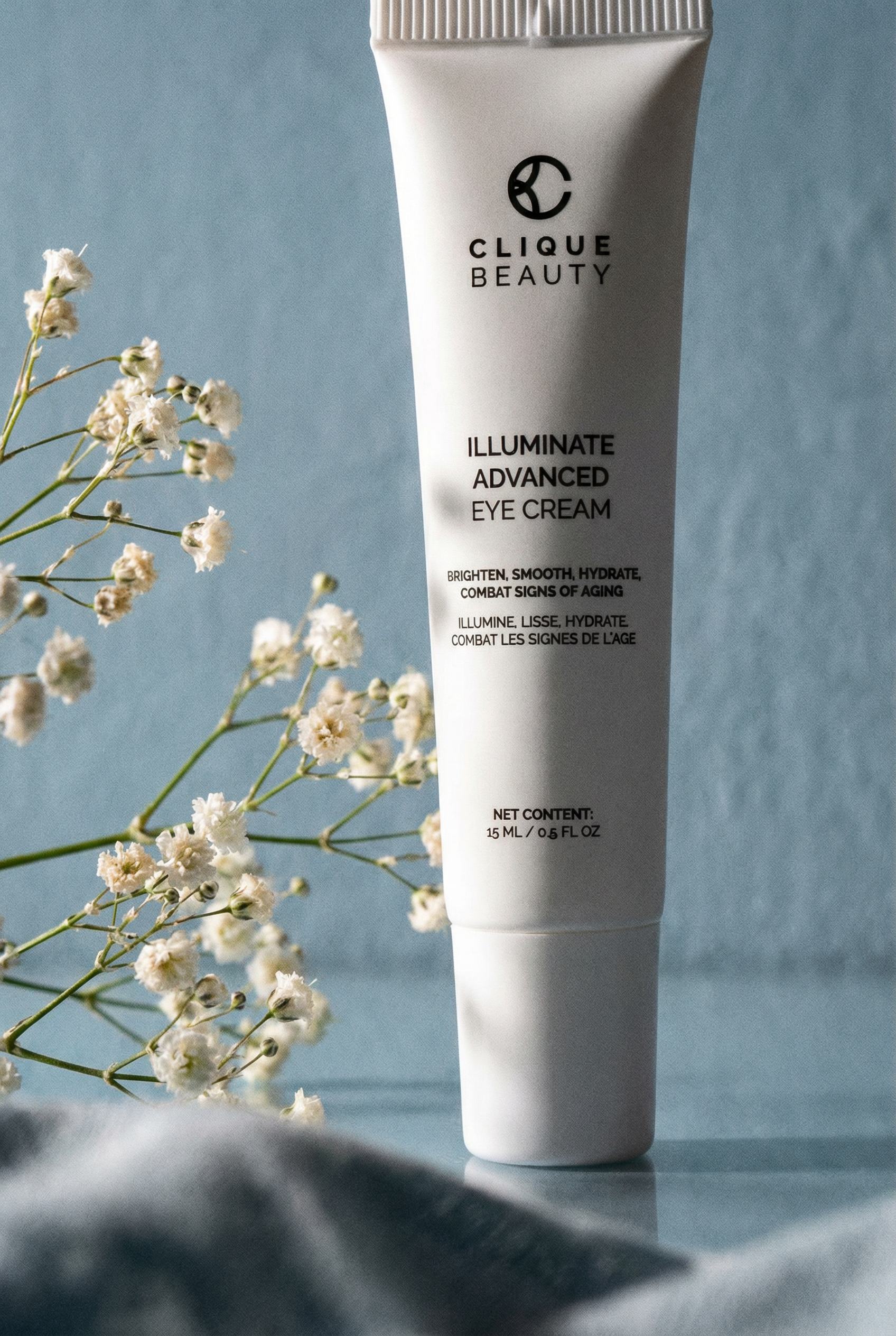 Tube of Clique Beauty Illuminate Advanced Eye Cream with flowers on a blue background